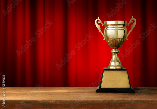 champion golden trophy on wood table with Red closed curtain bac