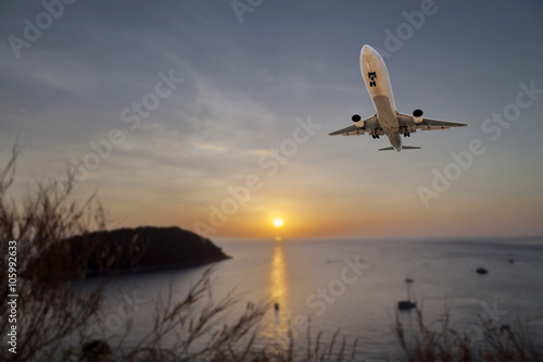 Airplane flying tropical sea at sunset time with reflection