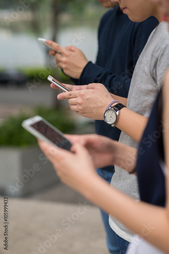 Teenagers with smartphones standing in row and using applications
