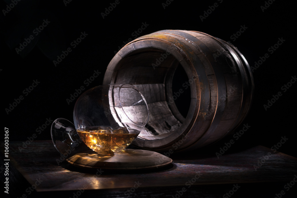 A glass of whiskey and ice against the backdrop of empty oak barrels A glass of whiskey and ice against the backdrop of empty oak barrels