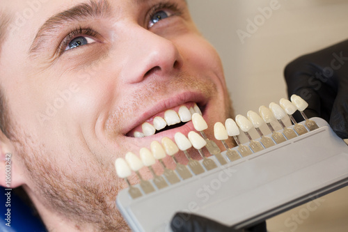 Close up portrait of Young man in dentist chair, Check and select the color of the teeth. Dentist makes the process of treatment in dental clinic office