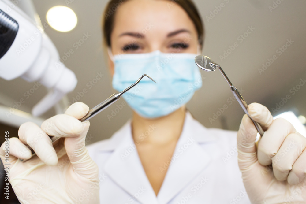 young women dentist with sterile mask readily approaching a patient with dental instruments held in the hands protected with surgical gloves young dentist with sterile mask young women dentist with sterile mask readily approaching a patient with dental instruments held in the hands protected with surgical gloves young dentist with sterile mask