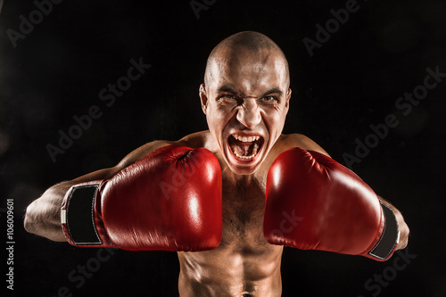 The young man kickboxing on black with screaming face