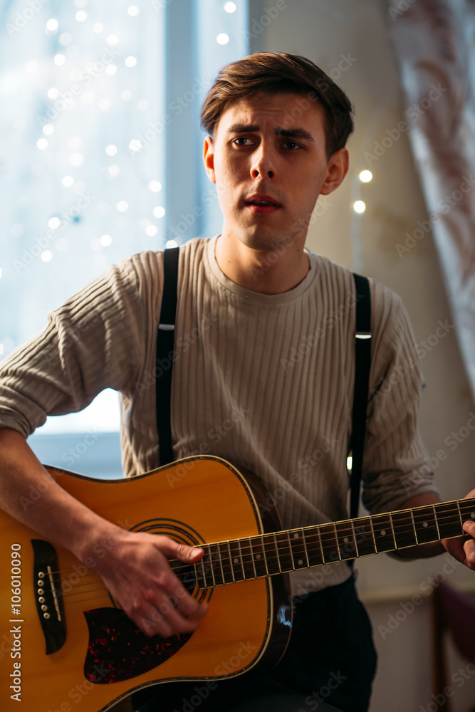 Obraz premium Young man sitting at home and playing guitar dramatic
