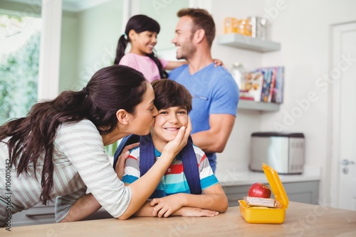 Mother kissing smiling son wearing schoolbag 