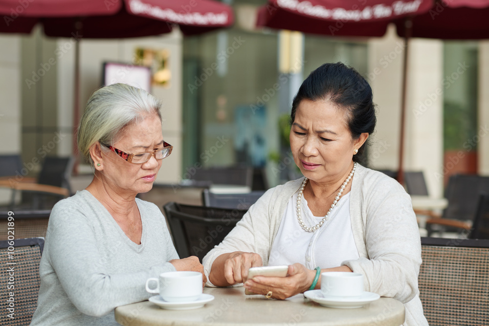 Asian senior woman sitting in cafe and discussing something on smartphone