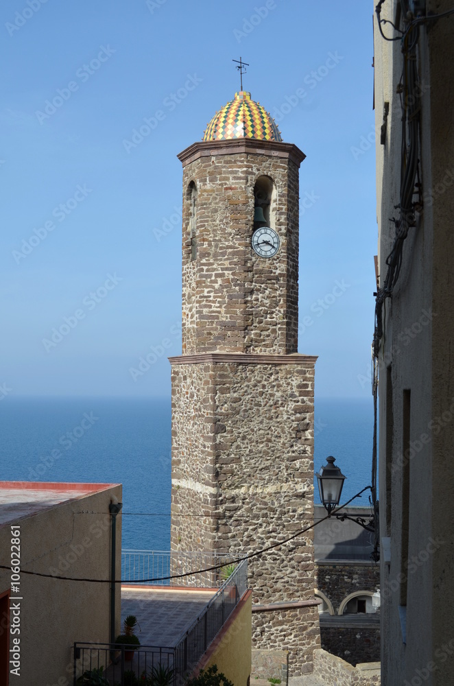 Vertical shot of Sant Antonio abate church bell tower in Castelsardo, Sardinia, Italy with blue sea view in back in a sunny day