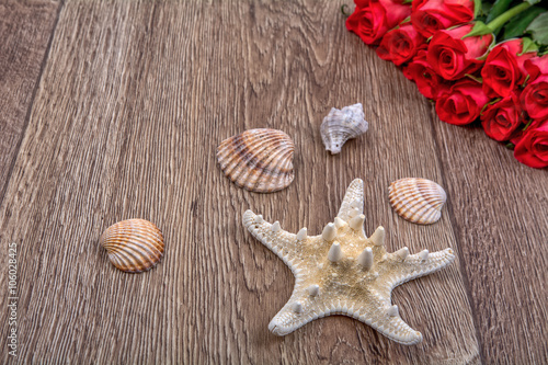 Starfish, shells and red roses on a wooden background