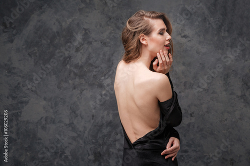 Alluring charming young woman in black dress with open back
