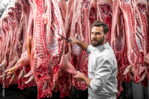 Handsome butcher cutting pork carcasse at the meat manufacturing