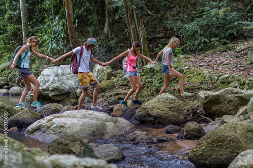 Young tourists are moving across the creek on the rocks in the jungle 