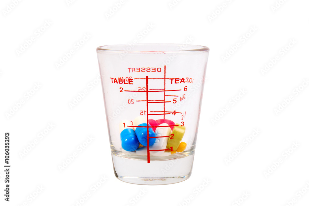 Many colorful pills in a measuring cup of glass on white background. Many colorful pills in a measuring cup of glass on white background.