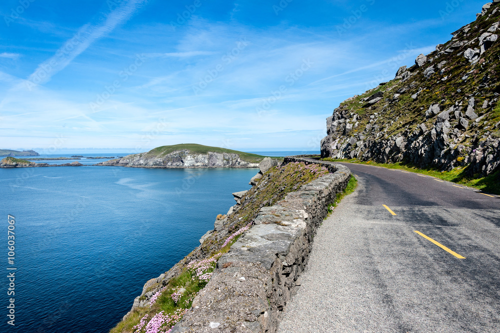 Ireland, Dingle, Slea Head: Street scene with panoramic view over coast, ocean water, bending empty street, the hill of Slea Head and blue sky in the background
