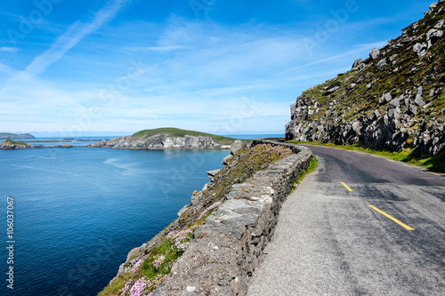 Ireland, Dingle, Slea Head: Street scene with panoramic view over coast, ocean water, bending empty street, the hill of Slea Head and blue sky in the background
