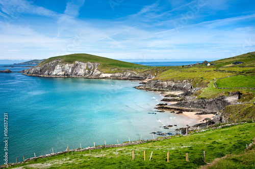 Ireland, Dingle, Slea Head: Coastal scene with panoramic ocean water view, bending coast line, green hill of Slea Head, horizon and blue sky in the background