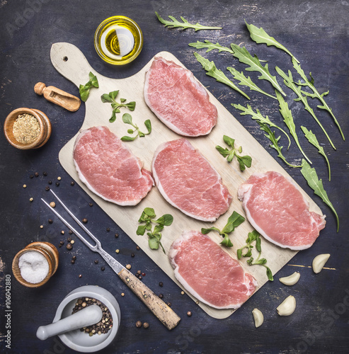 Raw Meat set Pork steaks with herbs and spices on a white cutting board on wooden rustic background top view