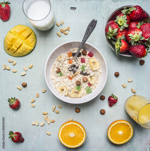 vitamin-rich breakfast, oatmeal with nuts and dried fruits, strawberries and mango, fresh juice on wooden rustic background top view close up