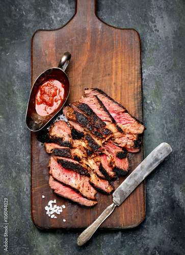 Sliced grilled Beef steak with knife and fork for meat on wooden cutting board
