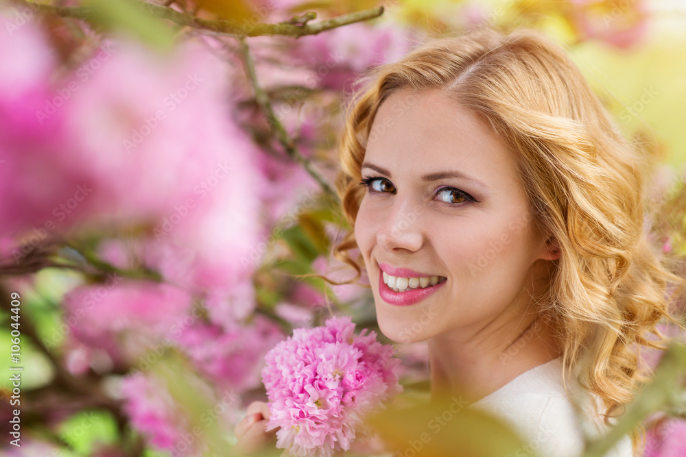 Blond woman, curly hair against pink tree in blossoom Blond woman, curly hair against pink tree in blossoom