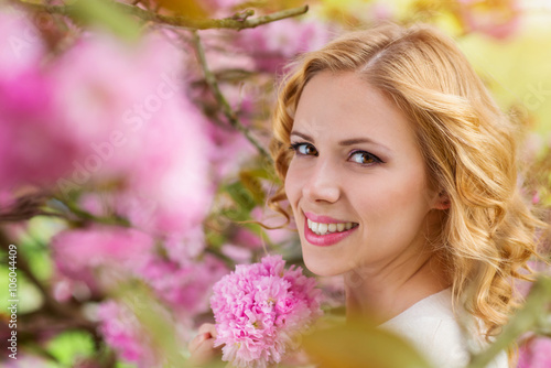 Blond woman, curly hair against pink tree in blossoom