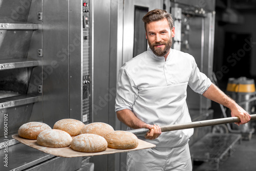 Canvastavla Handsome baker in uniform taking out with shovel freshly baked buckweat bread fr