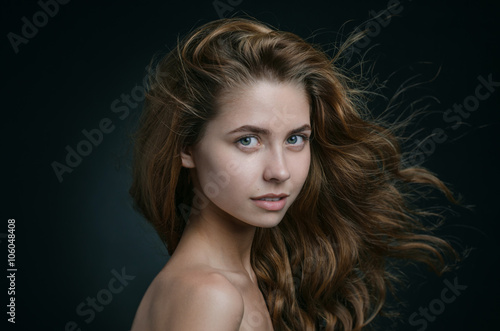 Dramatic portrait of a girl theme: portrait of a beautiful girl with flying hair in the wind against a background in studio