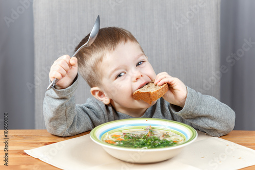 Funny kid with piece of bread and plate of soup
