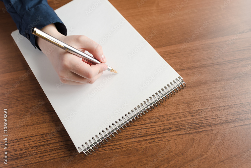 Пишет в пустой тетради ручкой, вид сверху сбоку