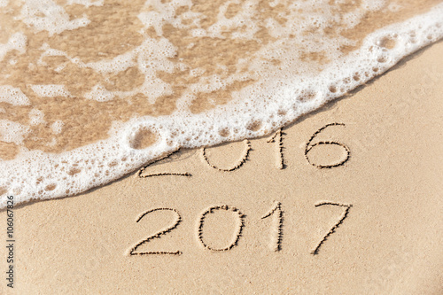 2016 2017 inscription written on wet yellow beach sand being washed by sea wave