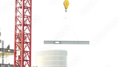 Tower crane moving I-beam, logos and faces blurrred