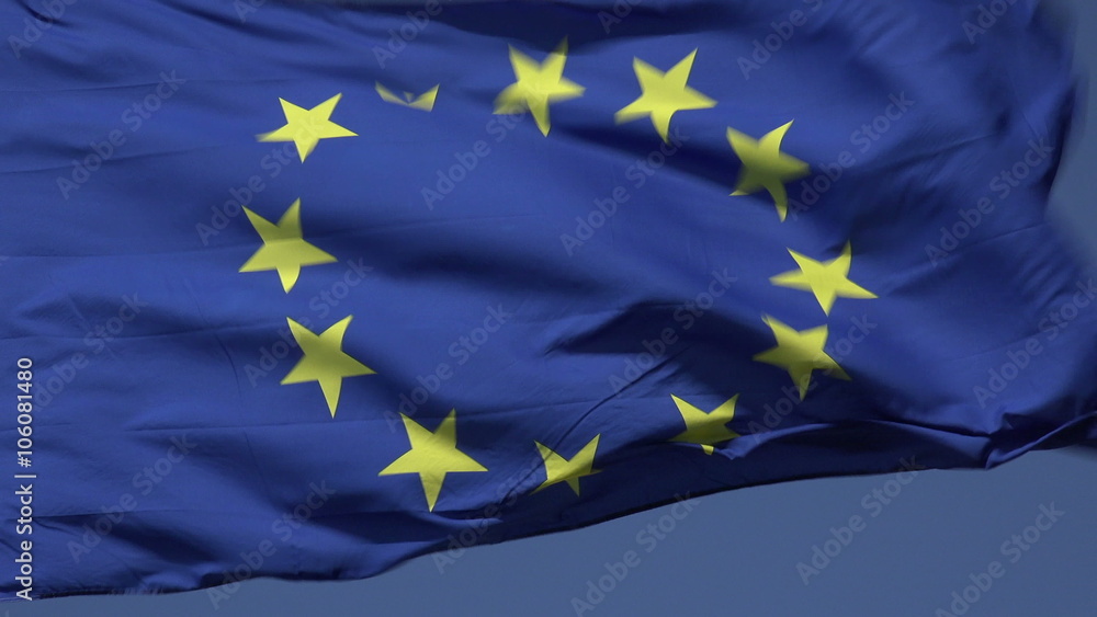 Zoom out, EU flag blowing in wind with blue sky background, European Union