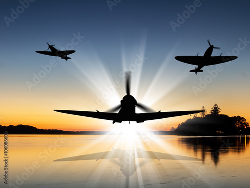 Fotografie Silhouette of Vintage British World War 2 fighters flying low over a river at sunrise - Artists Impression
