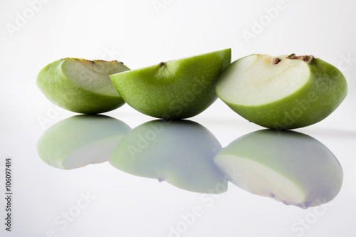 Sliced green apple half and two quarters on white background from side with reflection