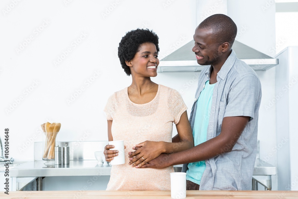 Pregnant couple embracing while having cup of coffee Pregnant couple embracing while having cup of coffee