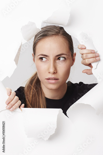 Curious woman looking through ripped paper