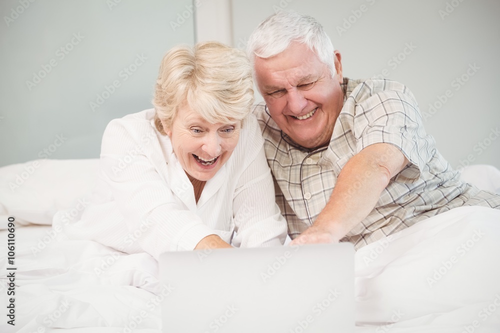 Couple laughing while using laptop in bed Couple laughing while using laptop in bed