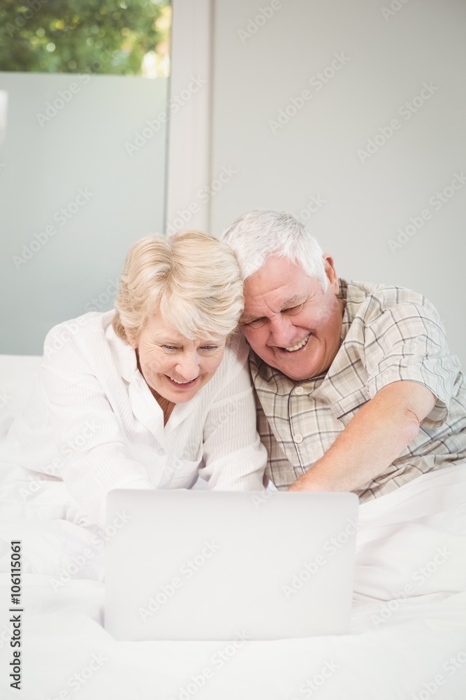 Happy couple laughing while using laptop in bed Happy couple laughing while using laptop in bed