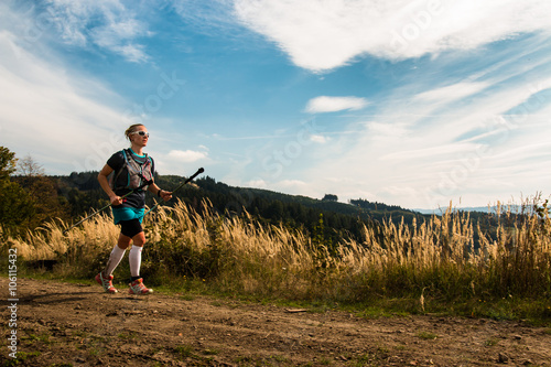 female ultra trail runner with poles training in the mountains with blue sky