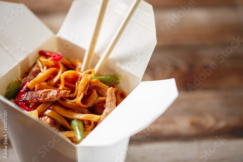 Noodles with pork and vegetables in take-out box on wooden table