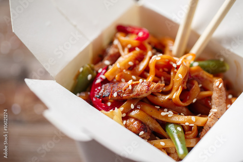 Noodles with pork and vegetables in take-out box on wooden table photo