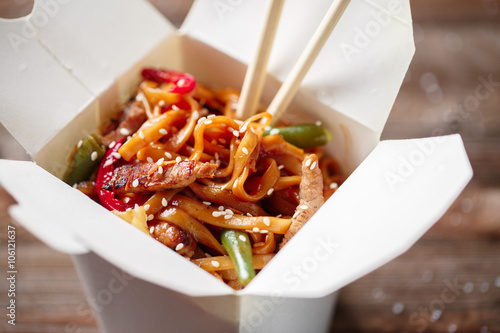 Noodles with pork and vegetables in take-out box on wooden table photo