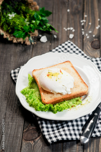 breakfast or lunch , poached egg and white toast , lettuce , herbs, salt and spices on a wooden background