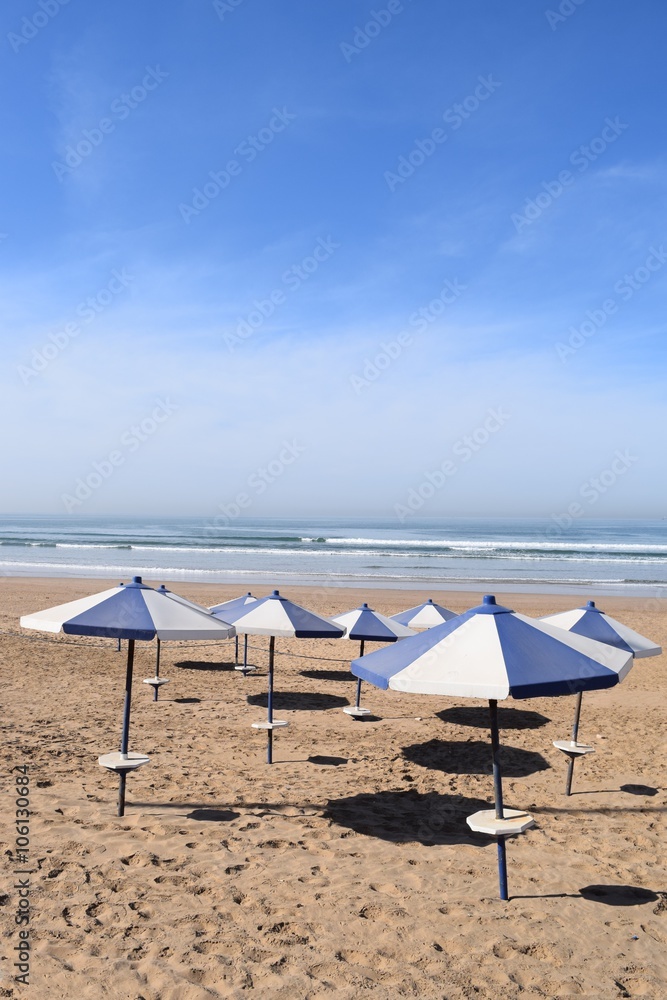 Fototapeta premium Sonnenschirme werfen kreisrunde Schatten auf den leeren Sandstrand am Atlantik