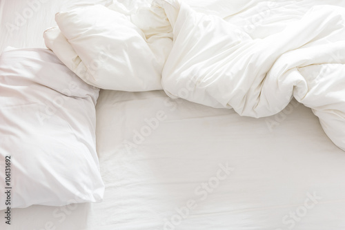 Top view of an unmade bed with a pillow, a bed sheet and a blanket after waking up in the morning.