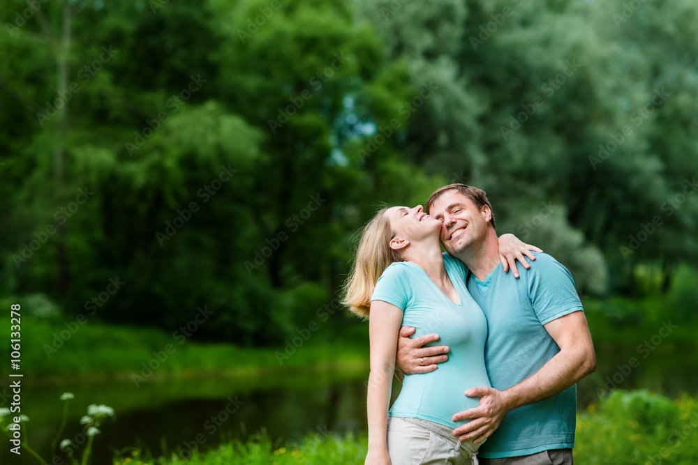 Smiling handsome man hugging his beautiful young pregnant woman and touching her belly in summer park. Happy family and pregnancy concept. Mother's Day Smiling handsome man hugging his beautiful young pregnant woman and touching her belly in summer park. Happy family and pregnancy concept. Mother's Day