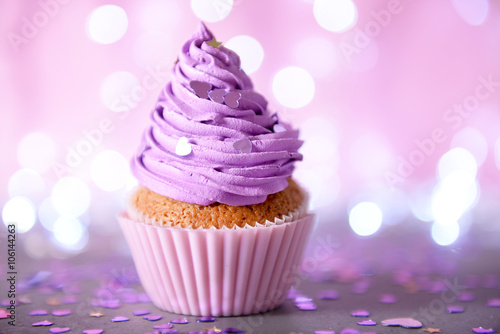 Cupcake with purple cream icing on a glitter background, close up