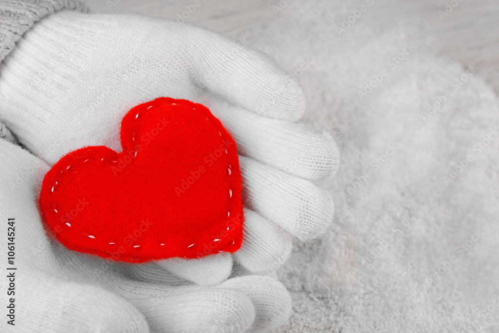 Fototapeta premium Hands in warm white gloves holding red heart on snowy background