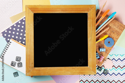Small school blackboard with stationery on colorful sheets of paper background