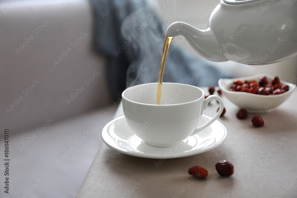 Fototapeta premium Pouring rose hip tea into cup, home atmosphere