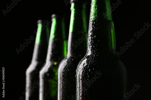Four green glass bottles of beer on dark background, close up